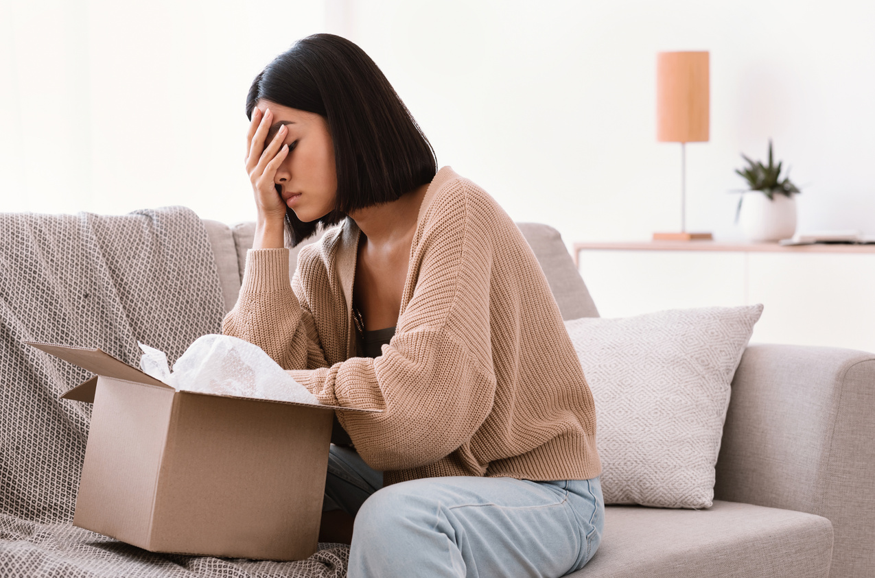 Sad young lady unpacking wrong parcel, delivery mistake